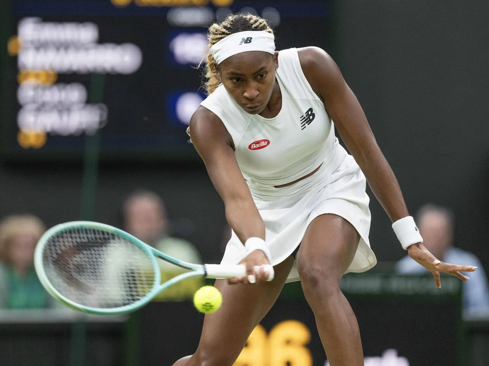 Coco Gauff hits a forehand slice low to the ground wearing all-white tennis gear.