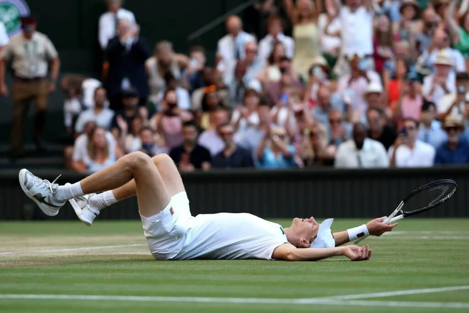 Jannik Sinner lies on his back on a grass court in celebration.