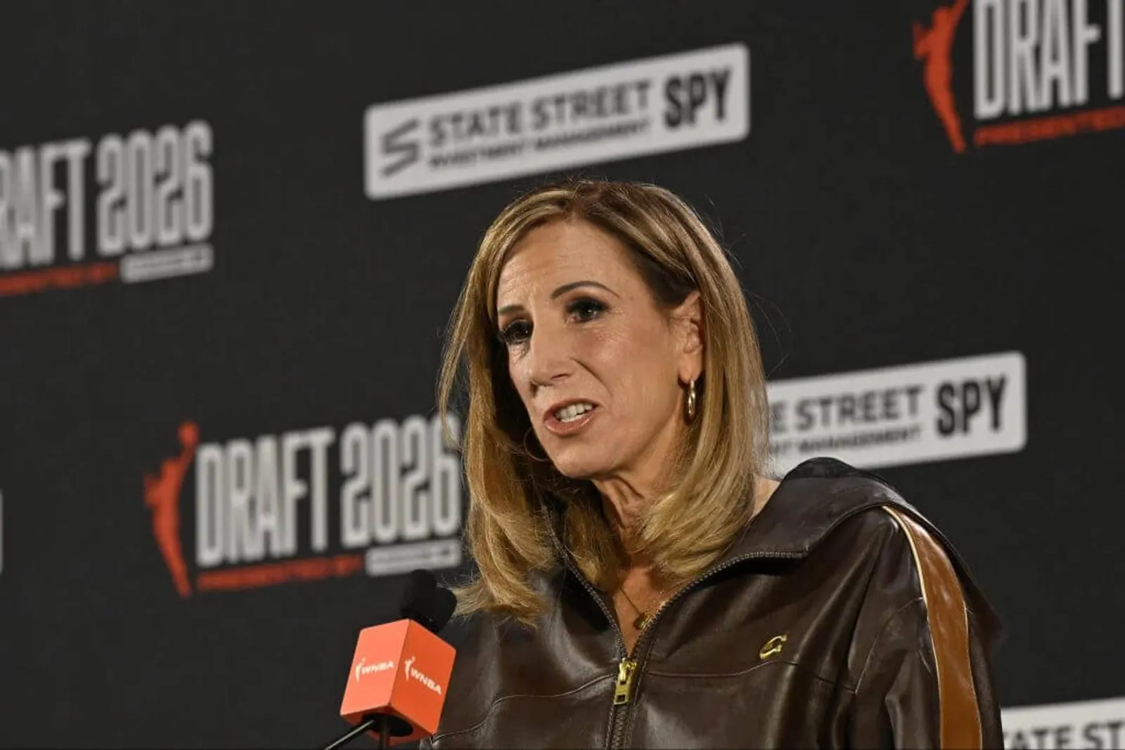 WNBA Commissioner Cathy Engelbert speaks into a microphone with a league logo on it at a news conference before the 2026 draft in April.
