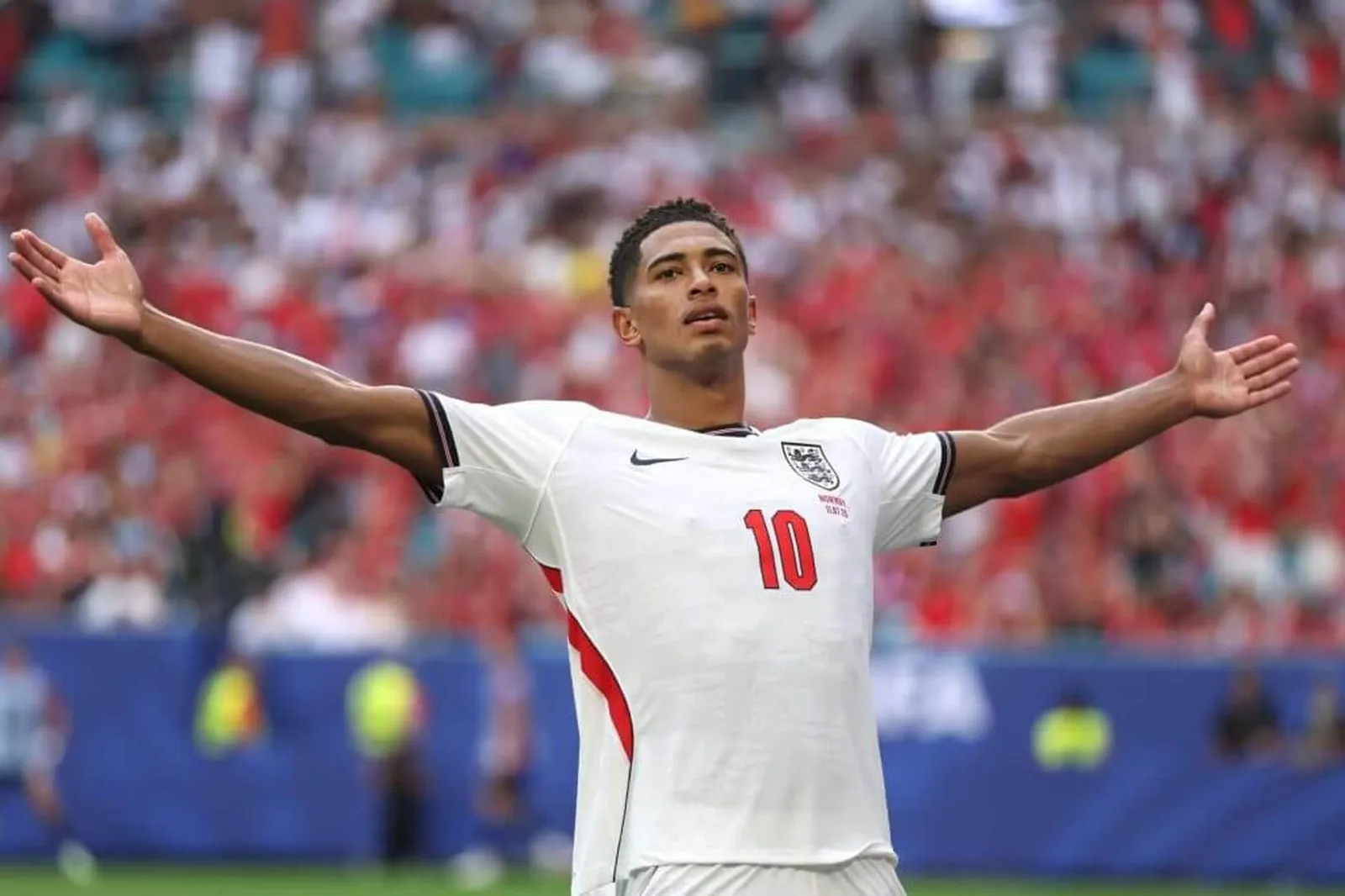 Jude Bellingham stands with his arms outstretched after scoring for England
